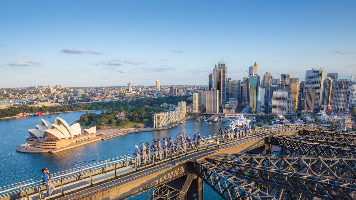 A group of people climb Sydney Harbour Bridge looking down towards the opera house and Circular Quay.